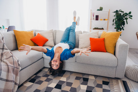 Photo of positve cheerful girl lying on couch upside down have fun living room dormitory indoorsの写真素材