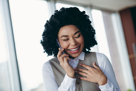 Smiling Successful Businesswoman Engaged in a Lively Phone Call Inside an Office Settingの写真素材