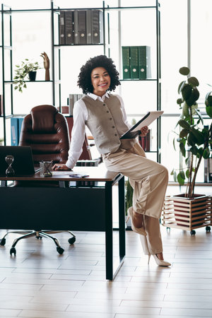 Young professional businesswoman standing confidently in a modern office environment with formal attire and a cheerful demeanorの写真素材