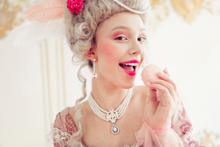 Young woman in elegant historical costume and intricate hairstyle enjoying a sweet treat in natural...