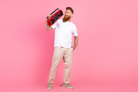 Young man with a stylish red beard holding a boombox against a pink background, showcasing casual...
