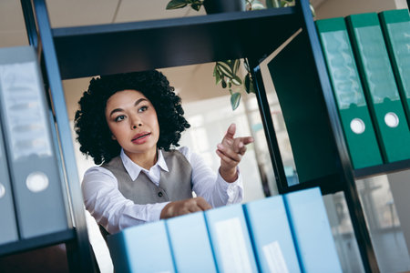 Young professional businesswoman organizing files in a modern office setting, showcasing professionalism and workplace dedicationの写真素材