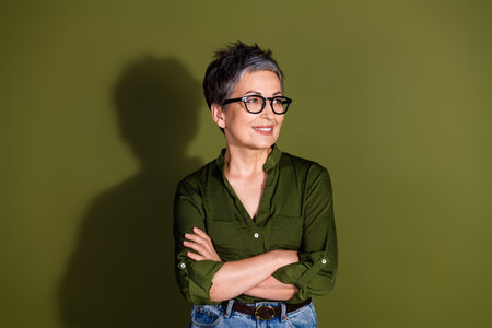 Confident mature woman with glasses in casual style posing against khaki background with arms crossed and a bright smileの写真素材