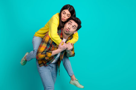 Happy young couple enjoying playful moments against a teal background, embracing and sharing joyful expressions in casual clothing.の写真素材