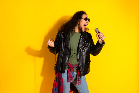 Energetic young man singing with a microphone on vibrant yellow background wearing stylish fashion leather jacketの写真素材