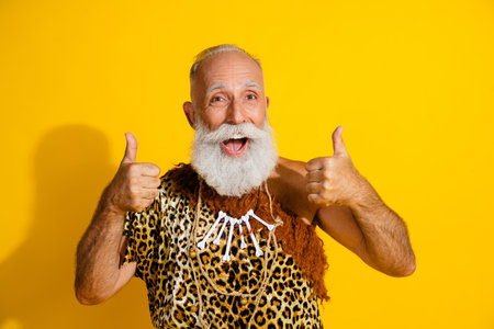 Photo of ancient aged caveman show thumb up wear leopard skin clothes isolated on yellow color...