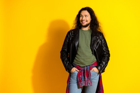 Attractive man with long black hair wearing a leather jacket posing against a vibrant yellow background in casual attireの写真素材