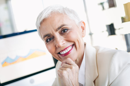 Confident mature businesswoman with short hair smiling in professional office setting, showcasing elegance and successの写真素材