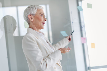Elegant senior businesswoman presenting ideas during a professional meeting in a modern office with confident expressionの写真素材