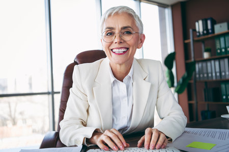 Elegant senior businesswoman smiling confidently in a modern office environment showcasing professionalism and warmthの写真素材
