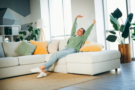 Lovely woman in a cozy home environment relaxing on a sofa during the daytime, enjoying comfort and mixing casual styleの写真素材