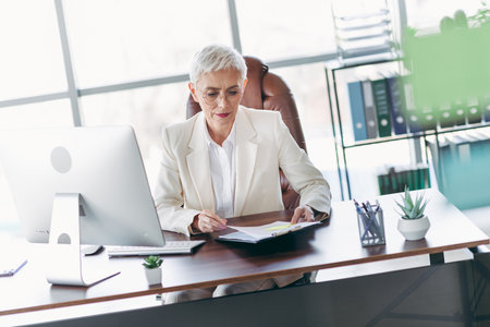 Senior professional businesswoman working at office desk in corporate workspace, focused and efficientの写真素材