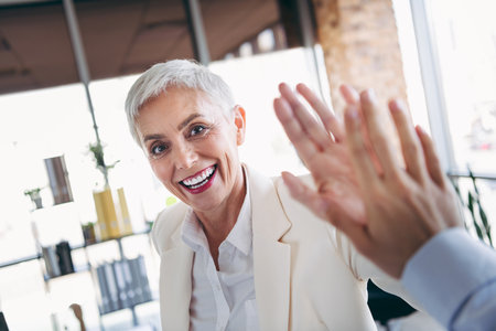 Confident senior professional celebrating success with a high five in a bright modern office environmentの写真素材