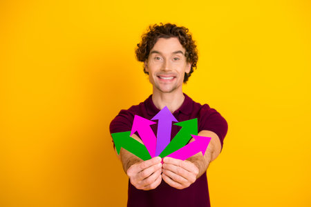 Young man holding colorful arrows on yellow background, expressing decision-making and options in a...
