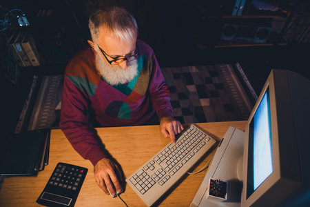 Elderly man working on computer at home office in the evening displaying focus and professionalism