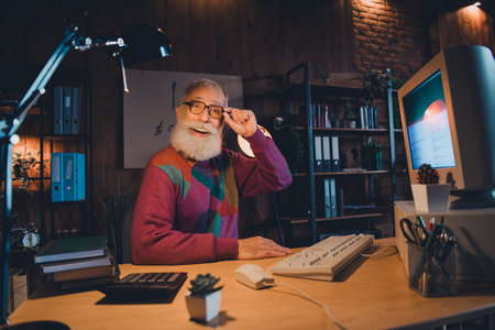 Elderly man working with a retro computer in a cozy home office showing cheerful expression under...