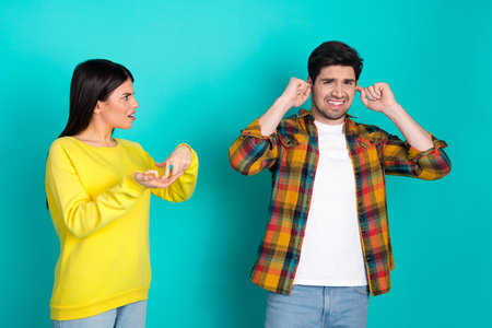 Young couple arguing with expressive gestures on a vibrant turquoise background highlighting...