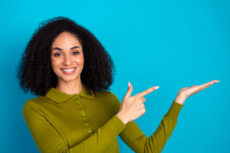 Smiling young woman in casual khaki shirt gesturing with hands against bright blue background, promoting lifestyle beautyの写真素材