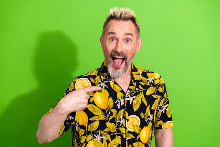 Playful bearded man in a vibrant lemon print shirt expressing joy on a green background