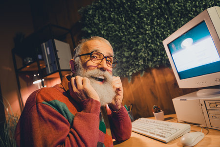 Happy Senior Programmer Working on a Vintage Computer in a Cozy Home Office, Enjoying Technology and...