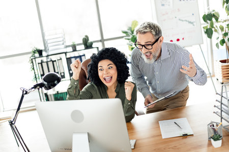Excited coworkers celebrating success while collaborating in a modern office environment, expressing...