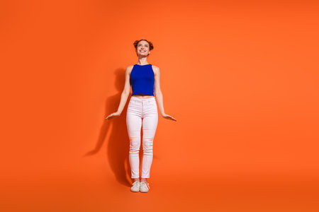 Young cheerful woman in casual summer outfit posing confidently against a vibrant orange backgroundの写真素材