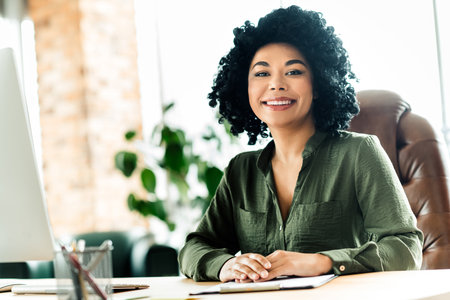 Confident young woman seated at a desk in a modern office environment symbolizing professionalism and positivityの写真素材