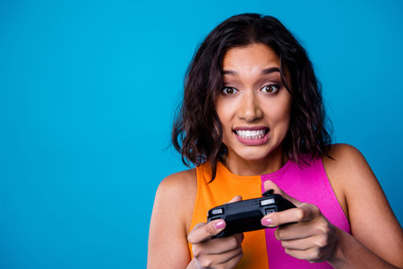 Young woman holding a gaming controller, smiling and engaged with intense focus on a vibrant blue...