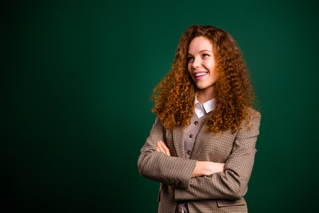 Confident professional woman in formal attire posing against an emerald green background with lively expressionの写真素材