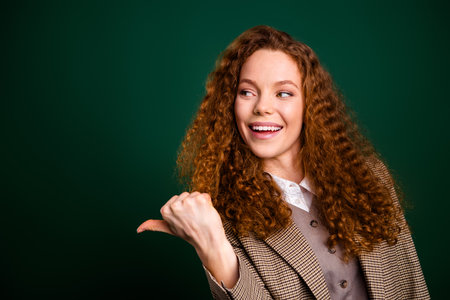 Young professional businesswoman with red curly hair showing exciting expression on elegant green backgroundの写真素材