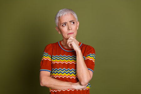 Contemplative mature woman with short white hair posing against green background wearing a colorful...