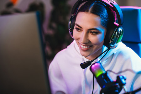 Positive woman gaming online with headset, illuminated by neon lights, streaming engaging content in...
