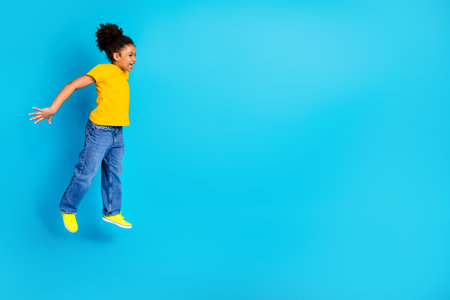 Joyful young girl jumping against a bright blue background, expressing happiness, energy, and positivityの写真素材