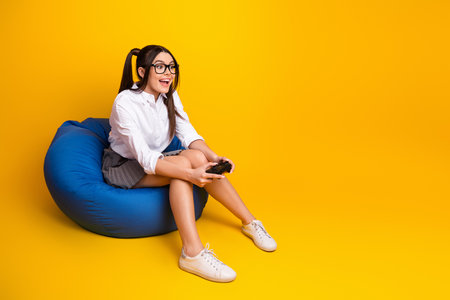 Smiling young woman holding a gaming controller while sitting on a blue beanbag chair against a...