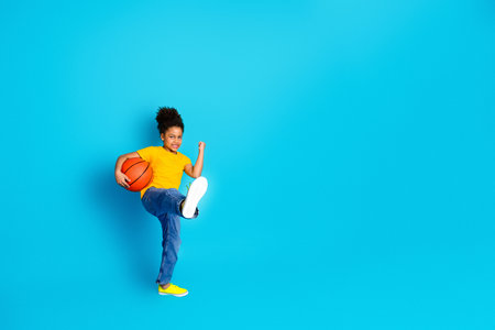 Young girl joyfully holding a basketball, posing confidently on a vibrant blue background, expressing energy and motionの写真素材