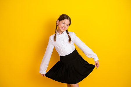 Stylish schoolgirl wearing a formal uniform posing against a vibrant yellow background, showcasing her charismatic charm.の写真素材