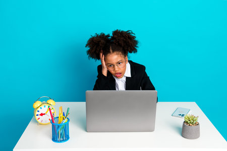 Portrait of a young girl working with a laptop, surrounded by school supplies on a teal background