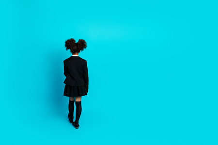 Back view of a schoolgirl standing against a teal background, showcasing dark hair, trendy attire, and formal styleの写真素材