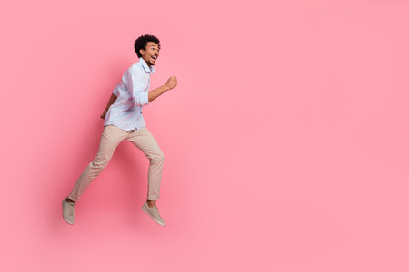 Energetic young man in casual attire joyfully leaping against a pink background showcasing style and enthusiasmの写真素材