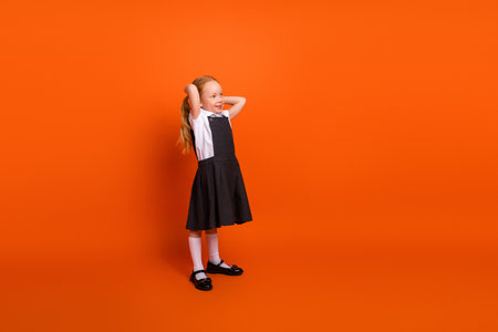 Cute schoolgirl in uniform with ponytails posing on bright orange background expressing happiness and joyの写真素材