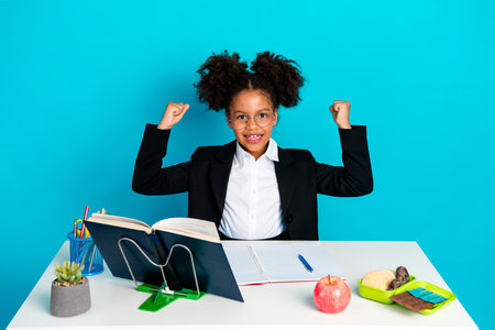 Confident young girl celebrating successful learning in a stylish office setting with book,...
