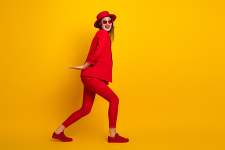 Stylish young woman in a vibrant red outfit posing dynamically against a bright yellow background, exuding confidence and charmの写真素材