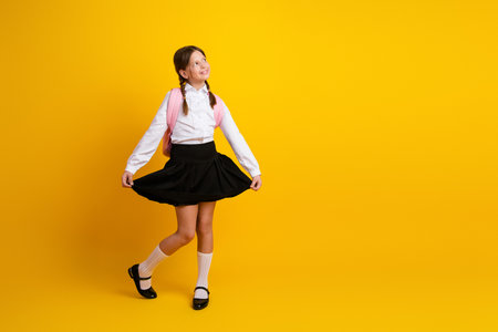 Charming Schoolgirl Twirling in Uniform on Yellow Background Showing Happiness and Excitement for a New School Yearの写真素材