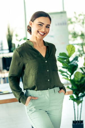 Confident professional businesswoman in formal attire at a modern office among plants and workspace elementsの写真素材