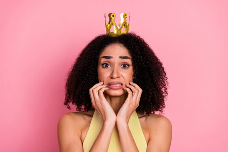 Charming young woman with a crown and curly hair posing on a pink background with a charming and girlish expressionの写真素材