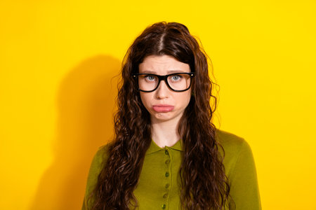 Young woman in glasses making a playful expression against a bright yellow background showcasing her...