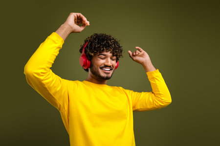 A cheerful young man enjoying music with wireless headphones, wearing trendy yellow apparel on a solid green backgroundの写真素材