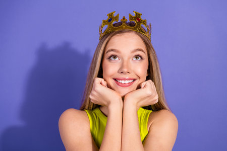 Young woman with crown smiling joyfully against a violet background exuding cheerful charm and a delightful youthful energyの写真素材