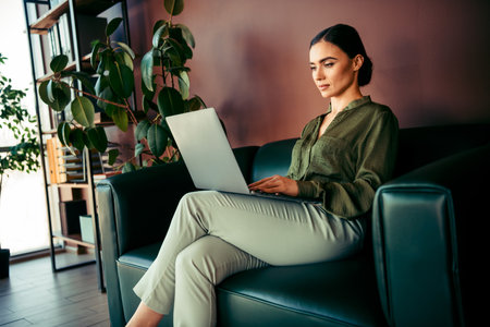 Young businesswoman working on her laptop in a stylish office environment, wearing elegant formal attire, focused and professionalの写真素材