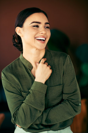 Young professional businesswoman smiling confidently in the office wearing a stylish green blouse, embracing successの写真素材